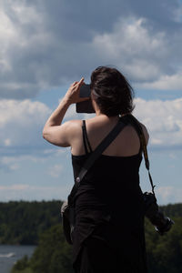 Rear view of woman photographing against cloudy sky