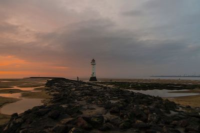 Lighthouse by sea against sky during sunset