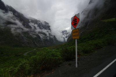 Road sign by mountains against sky