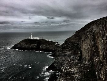 Lighthouse on cliff by sea against sky