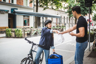 Food delivery woman giving package to male customer standing on sidewalk in city