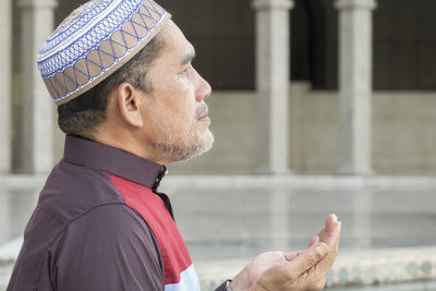 Close-up of mature man praying while sitting at mosque