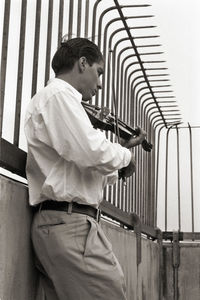 Side view of man playing violin by railing