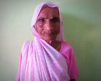 Close-up portrait of senior woman in sari standing against wall