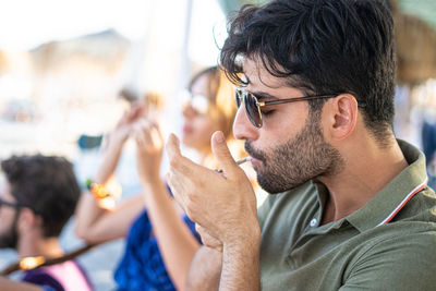 Portrait of young man holding eyeglasses while sitting outdoors