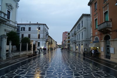 Wet street amidst buildings against sky during rainy season