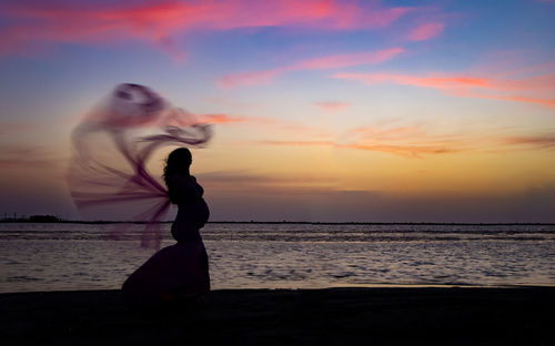 Woman standing on beach against sky during sunset