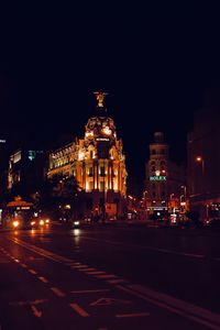 Illuminated building by street against sky at night