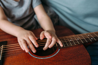 A cute kid plays with a big acoustic guitar at home