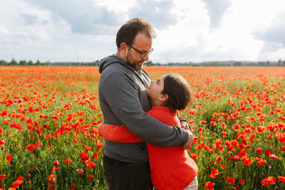 Father and daughter hugging each other on a sunny day in the big field of poppies