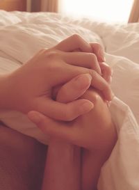 Cropped image of people holding hands on bed at home