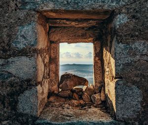 Stone wall by sea against sky seen through window