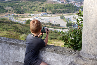 Side view of woman photographing while sitting on rock