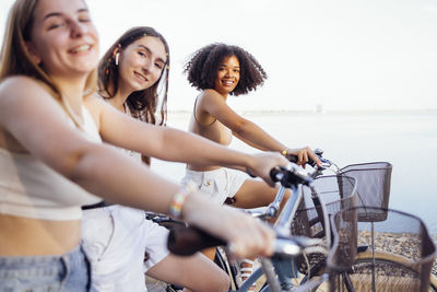 Portrait of smiling friends with bicycle against sky