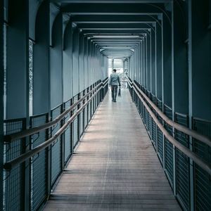 Rear view of man walking on bridge in building