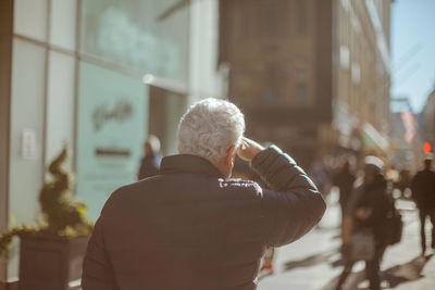 Rear view of man walking by buildings on sunny day