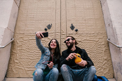 Man and woman smiling, making a selfie sitting in the city