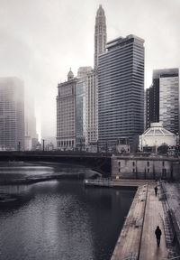 Modern buildings by river against sky in city