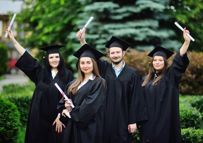 Portrait of smiling woman holding diploma standing by friends