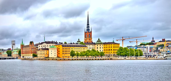 Buildings by river against cloudy sky