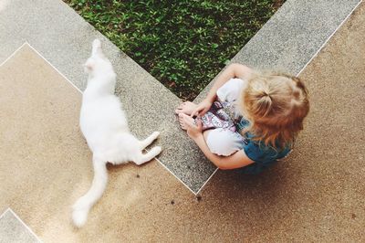 Directly above shot of girl sitting by cat on sidewalk