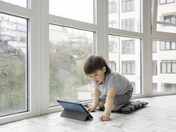 Curious boy watch cartoons on digital tablet. kid sits on floor and uses electronic device. indoors.