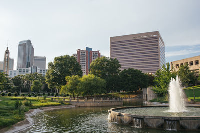 Fountain in park by buildings against sky in city