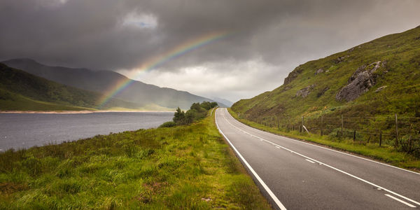 Scenic view of mountain road against rainbow in sky