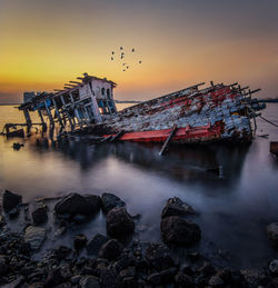 Ship wreck in sea against sky during sunset