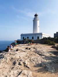 People by lighthouse against sky