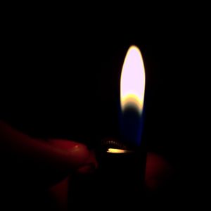 Close-up of hand holding illuminated candle in darkroom