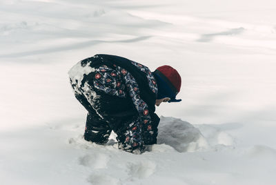 Side view of boy playing with snow on field