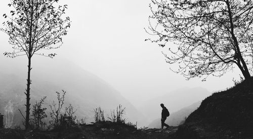 Side view of man walking on field against mountain during foggy weather