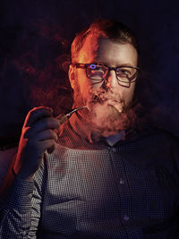 Portrait of mature man smoking while sitting against black background