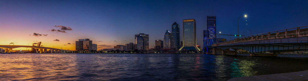 Illuminated bridge over river by buildings against sky in city