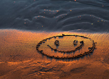 Close-up of anthropomorphic smiley face in sand on shore at beach during sunset