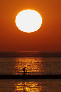 Silhouette man on sea against orange sky