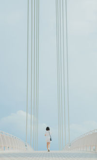 Rear view of woman walking on bridge against sky