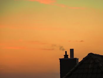 High section of silhouette building against orange sky