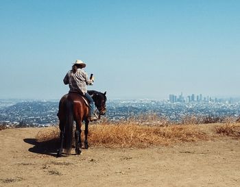 Rear view of cowboy sitting on horse against clear sky