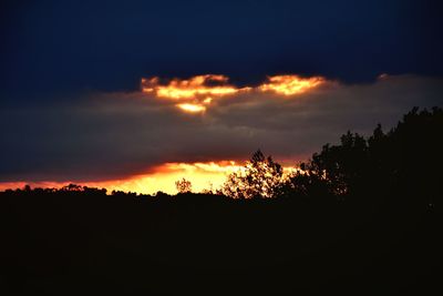 Silhouette trees against dramatic sky during sunset