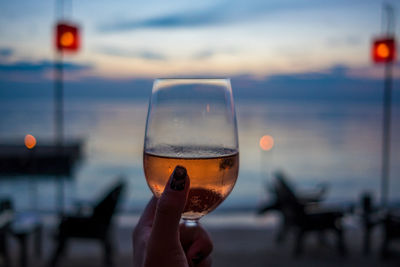 Close-up of hand holding wineglass against sea during sunset