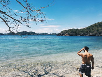 Rear view of shirtless man standing in sea against sky