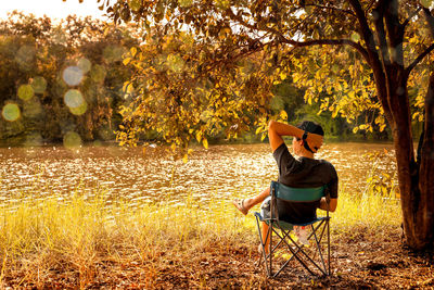 Rear view of man sitting on seat at lakeshore