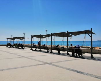 People sitting on beach against clear blue sky