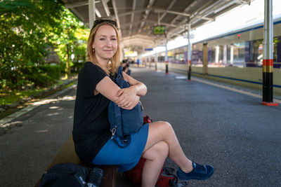 Portrait of smiling woman sitting on bench at railway station