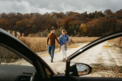 Happy man and woman are walking down a country road next to their car holding hands