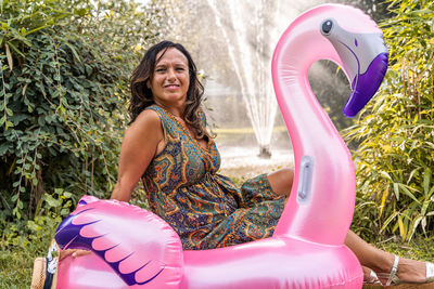Beautiful smiling middle aged woman having fun sitting on a pink flamingo shaped inflatable toy