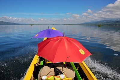 Canoe floating in lake against cloudy sky