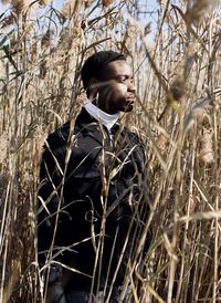 Young man looking away while standing amidst plants